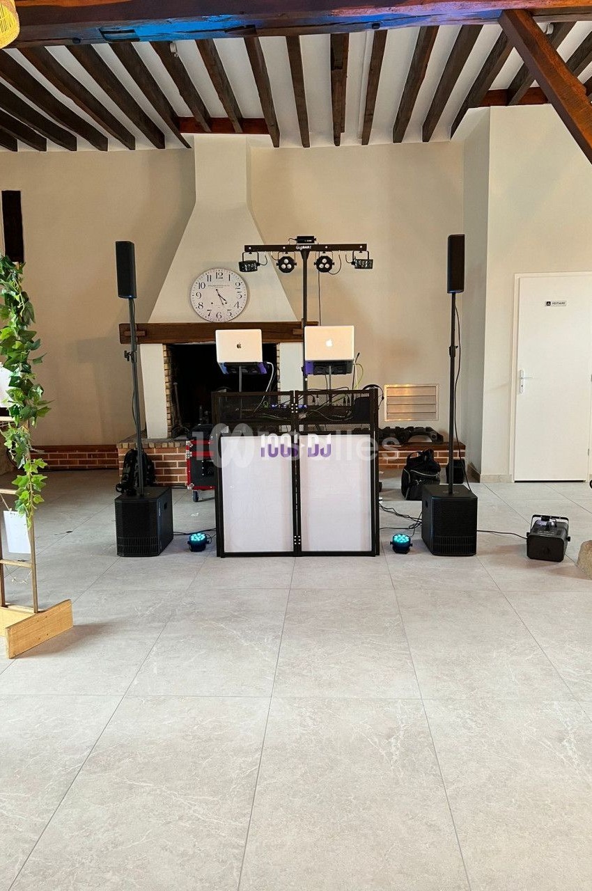 Installation de matériel de DJ avec enceintes, lumières et ordinateurs dans une salle avec poutres apparentes et cheminée.