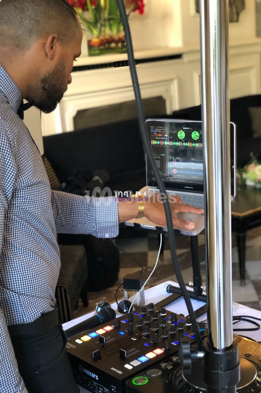Un DJ ajuste les réglages sur une table de mixage connectée à un ordinateur lors d'un événement en intérieur.
