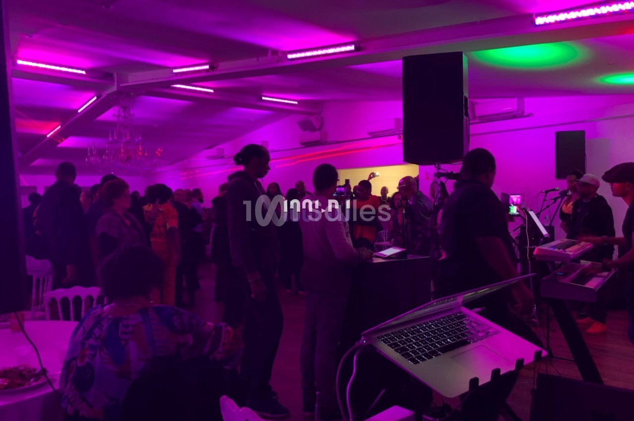 Groupe de personnes dans une salle éclairée par des lumières colorées, avec un DJ et du matériel audio visible au premier…