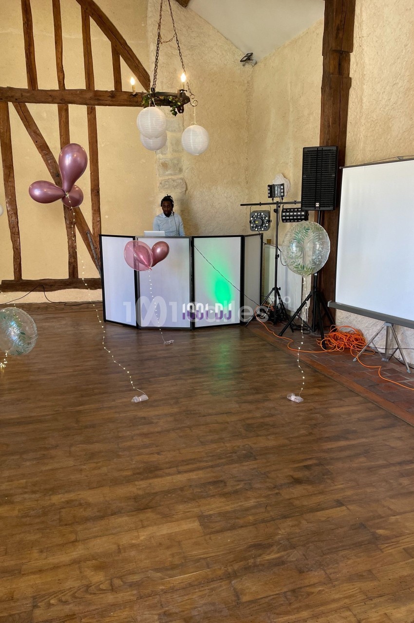 Salle de réception avec parquet, décorations de ballons, éclairage, et un DJ derrière une table lumineuse.