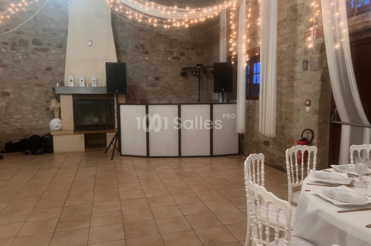Salle en pierre décorée de guirlandes lumineuses avec une table dressée et un espace DJ équipé de haut-parleurs.