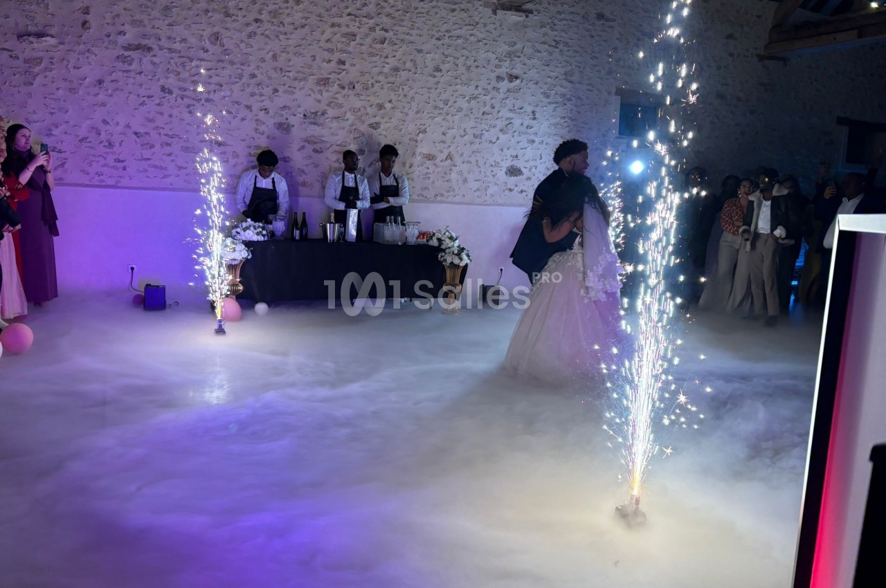Un couple danse dans une salle éclairée, entouré de fumée au sol et de fontaines d'étincelles.
