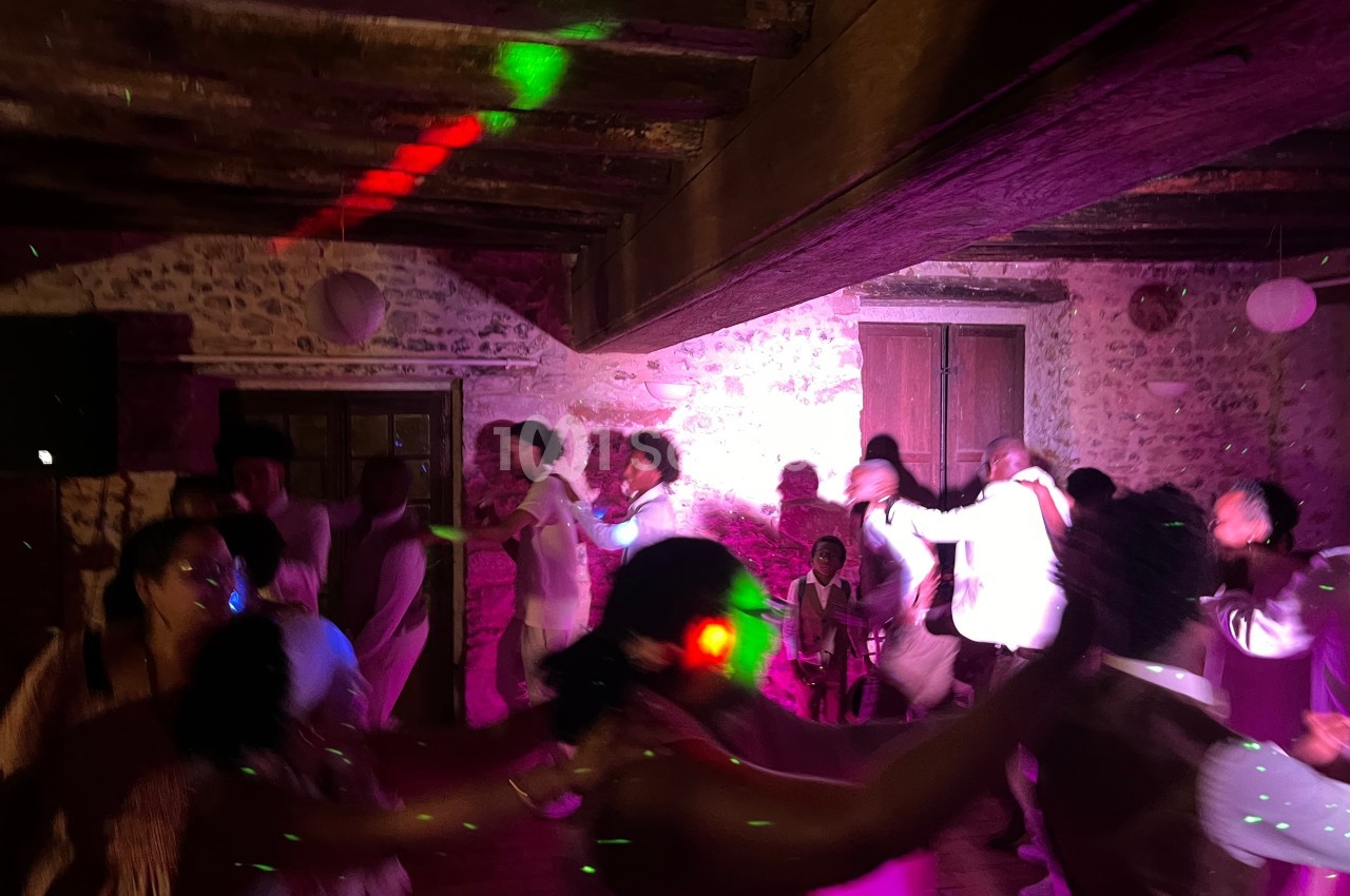 Des personnes dansent dans une salle en pierre éclairée par des lumières colorées, créant une ambiance festive.