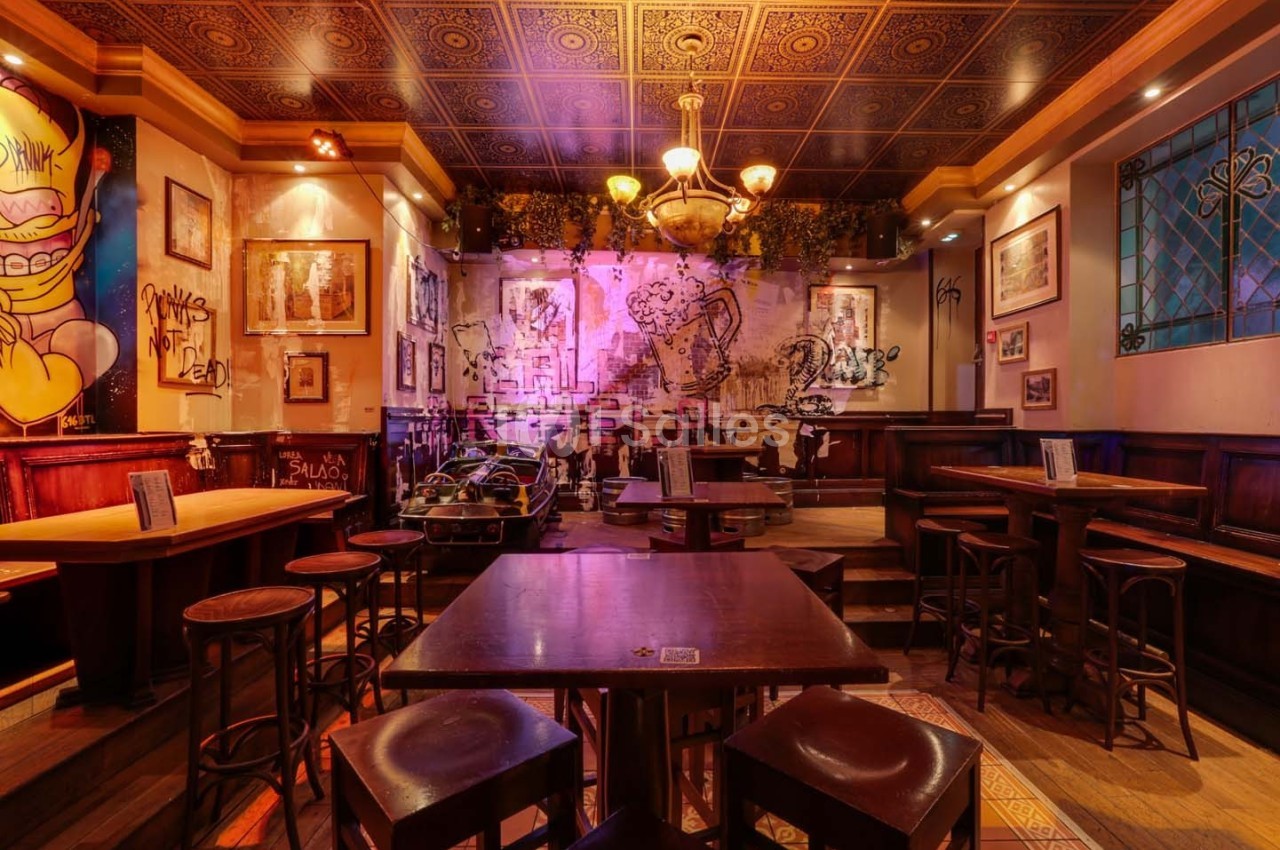 Intérieur d'un bar avec tables en bois, décorations murales artistiques et éclairage chaleureux.