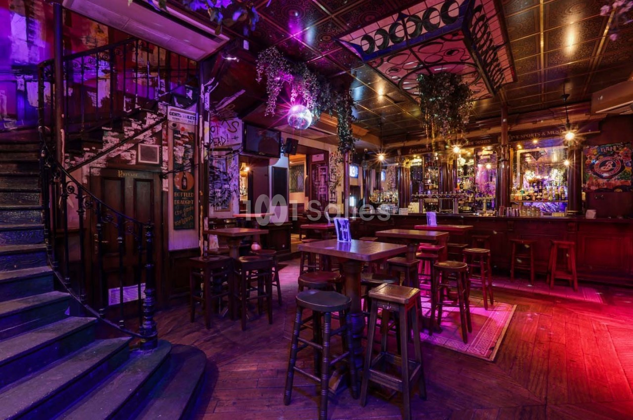 Intérieur d'un bar chaleureux avec éclairage tamisé, tables en bois, escalier en colimaçon et décorations suspendues.