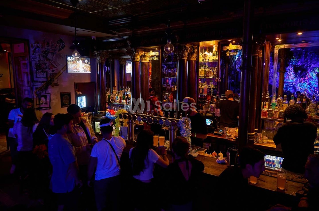 Des personnes discutent et commandent des boissons dans un bar à l'éclairage tamisé avec un comptoir en bois.