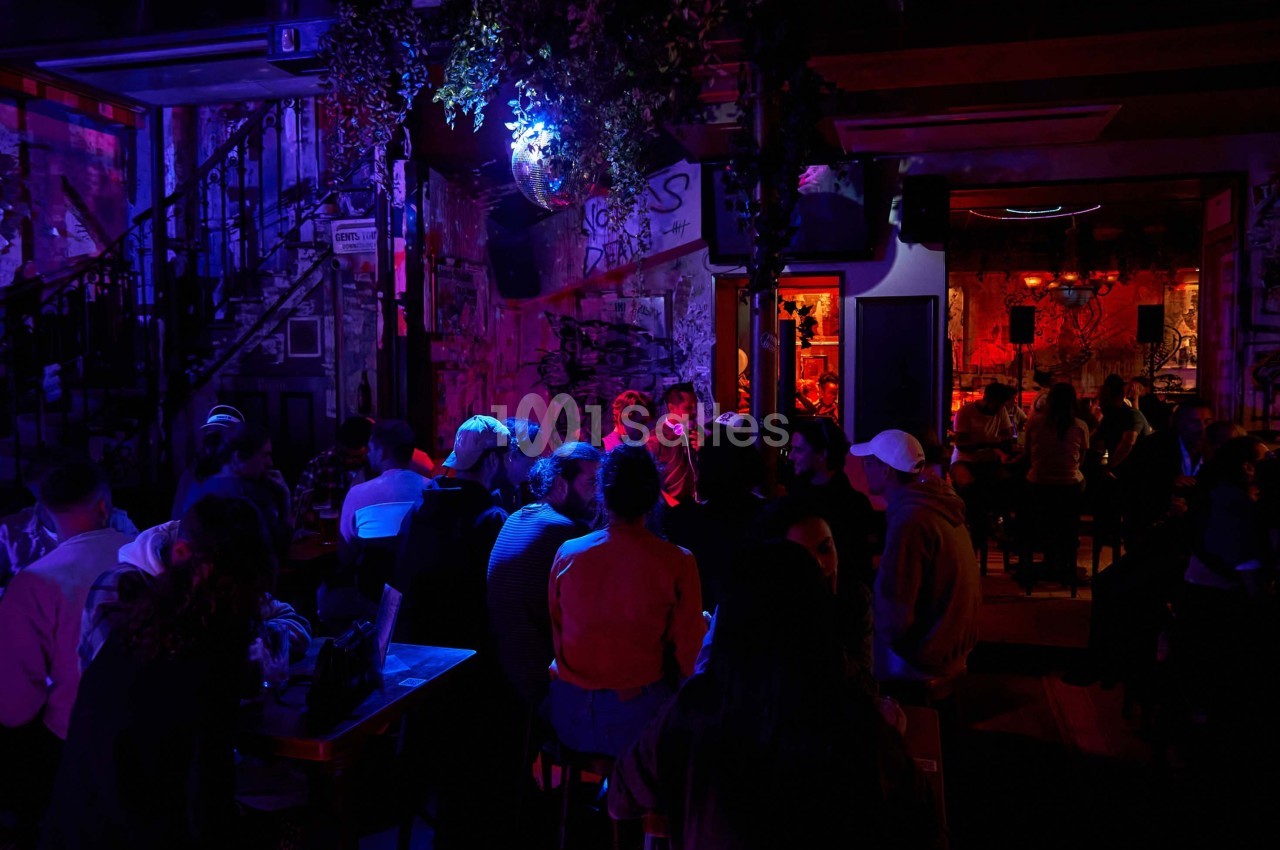 Groupe de personnes assises dans un bar à l'ambiance tamisée avec des lumières colorées et un décor urbain.