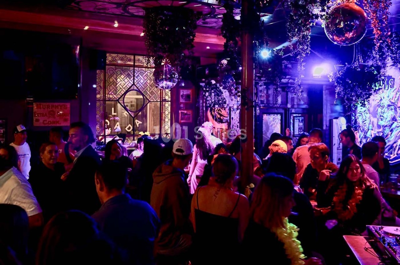 Personnes rassemblées dans un bar animé avec éclairage coloré, décorations suspendues et ambiance festive.