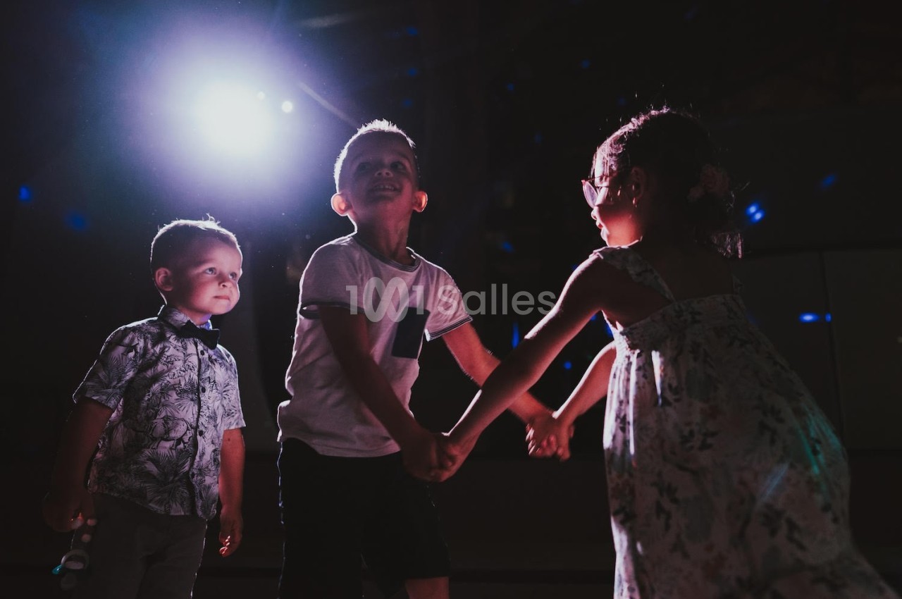 Trois jeunes enfants dansent ensemble sous une lumière vive dans un environnement sombre.