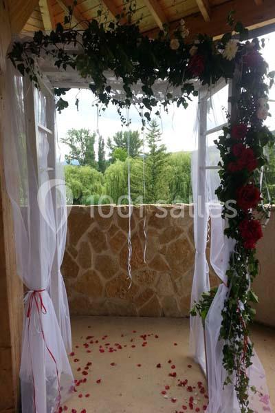 Arche de mariage décorée de fleurs rouges et blanches, entourée de voilages blancs, avec des pétales au sol.
