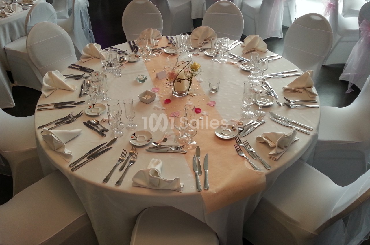 Table ronde élégamment dressée avec une nappe blanche, des couverts, des verres et une décoration centrale florale.