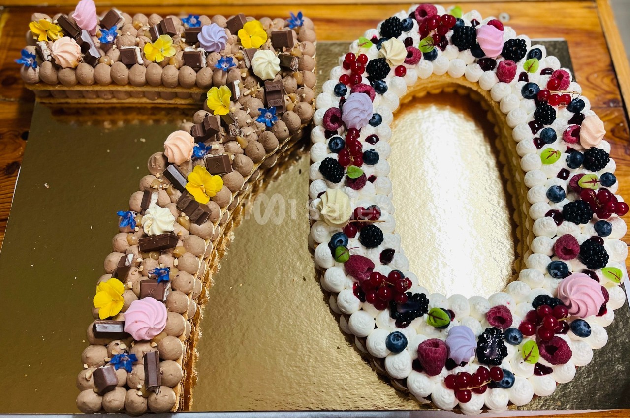 Gâteau en forme de ’70’ décoré de crème, fruits rouges, fleurs comestibles et morceaux de chocolat.
