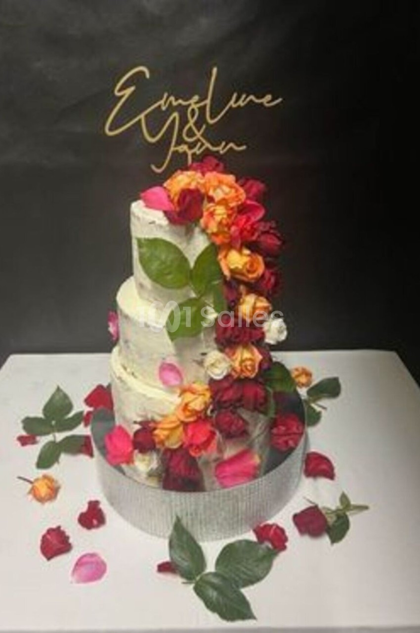 Gâteau de mariage à trois étages décoré de roses colorées et de feuilles, sur fond noir.