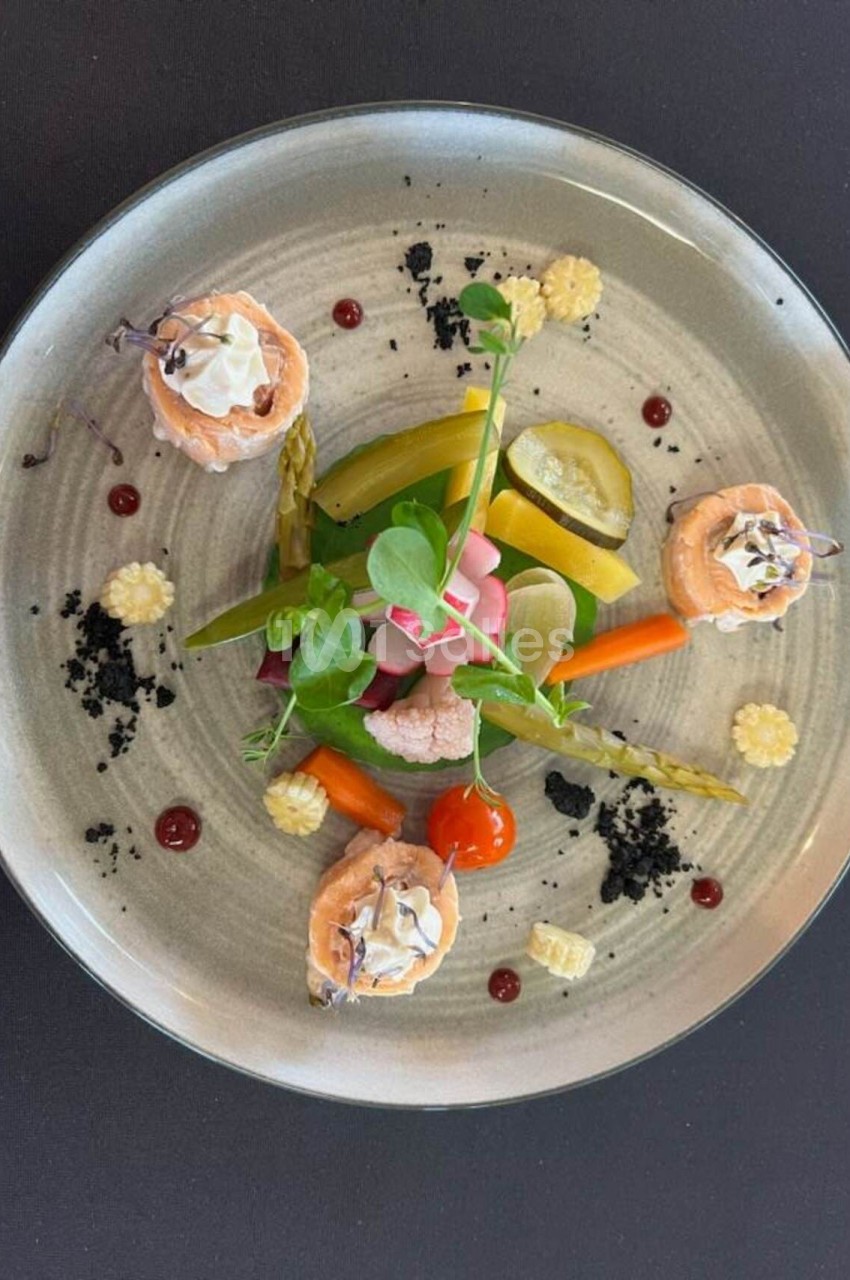 Assiette gastronomique composée de légumes colorés, saumon roulé et garnitures raffinées sur une table noire.
