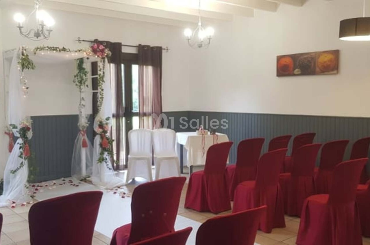 Salle décorée pour une cérémonie, avec une arche fleurie, des chaises rouges et un éclairage suspendu.