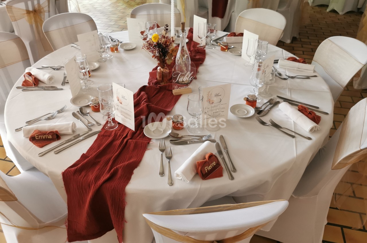 Table ronde décorée pour un événement, avec nappes blanches, chemins de table rouges, vaisselle et marque-places.
