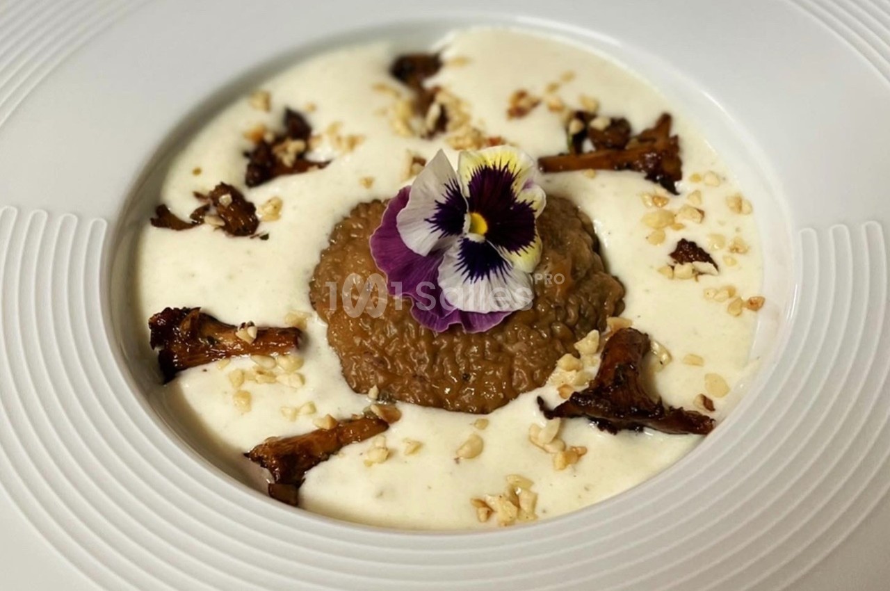 Plat gastronomique composé de risotto au centre, entouré de sauce crémeuse, champignons et décoré d'une fleur comestible.