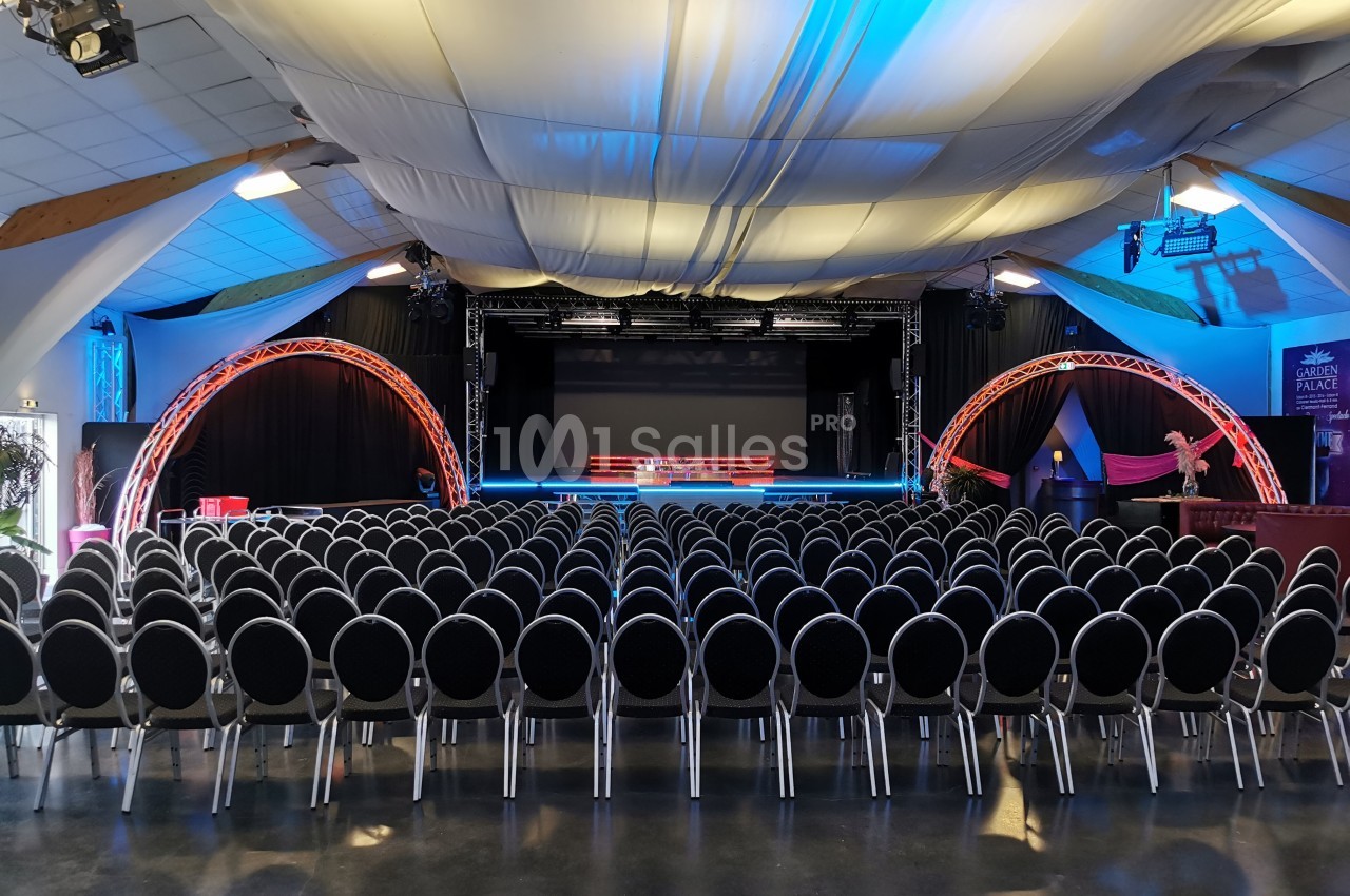 Salle de spectacle avec rangées de chaises noires alignées face à une scène éclairée par des projecteurs.