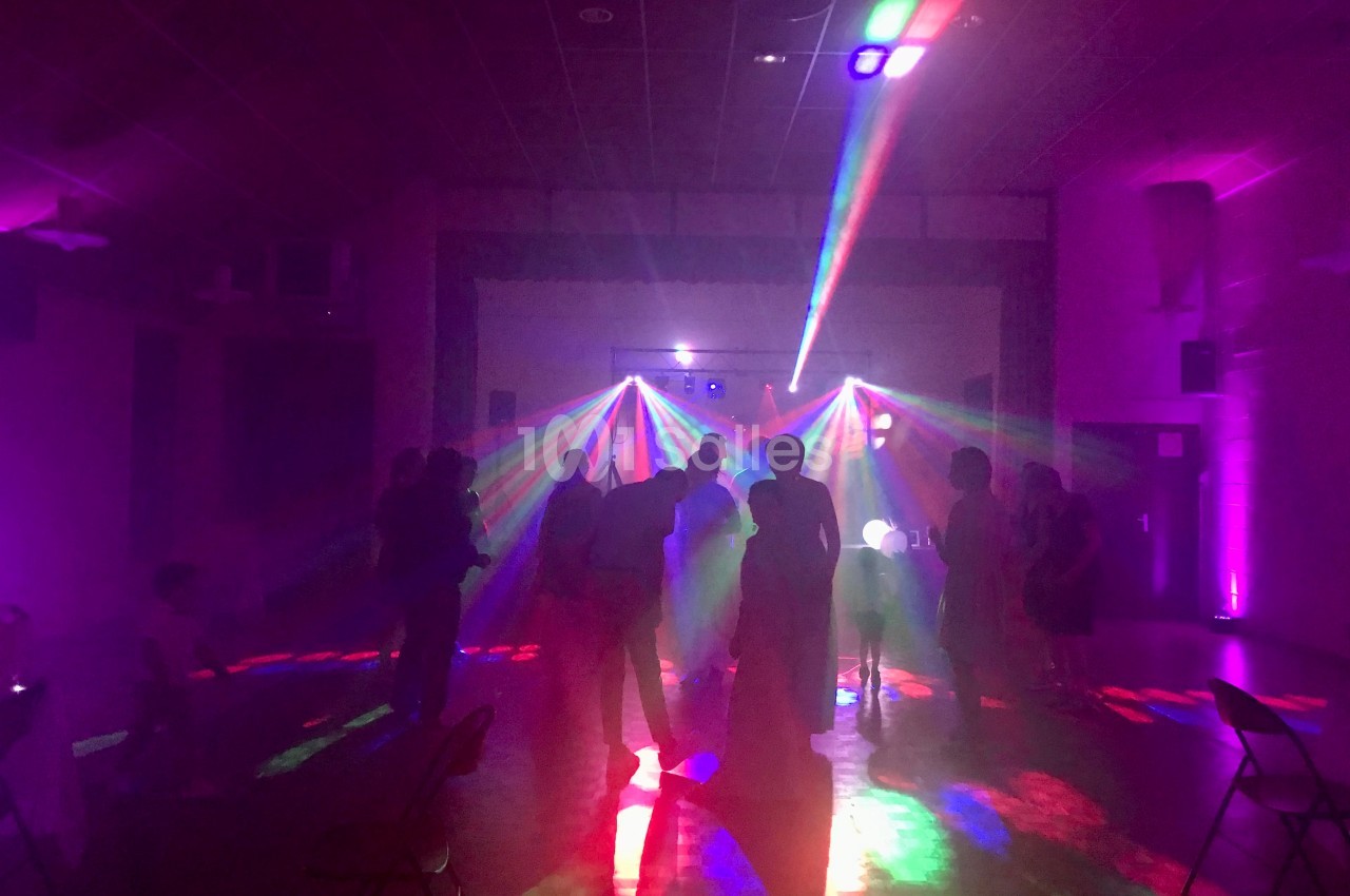 Personnes dansant dans une salle sombre éclairée par des faisceaux lumineux colorés provenant d'un jeu de lumières.