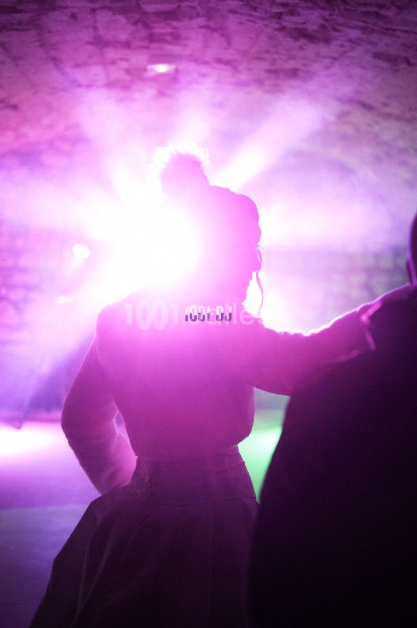 Personne de dos dans une ambiance lumineuse violette sous une voûte, éclairée par des projecteurs.