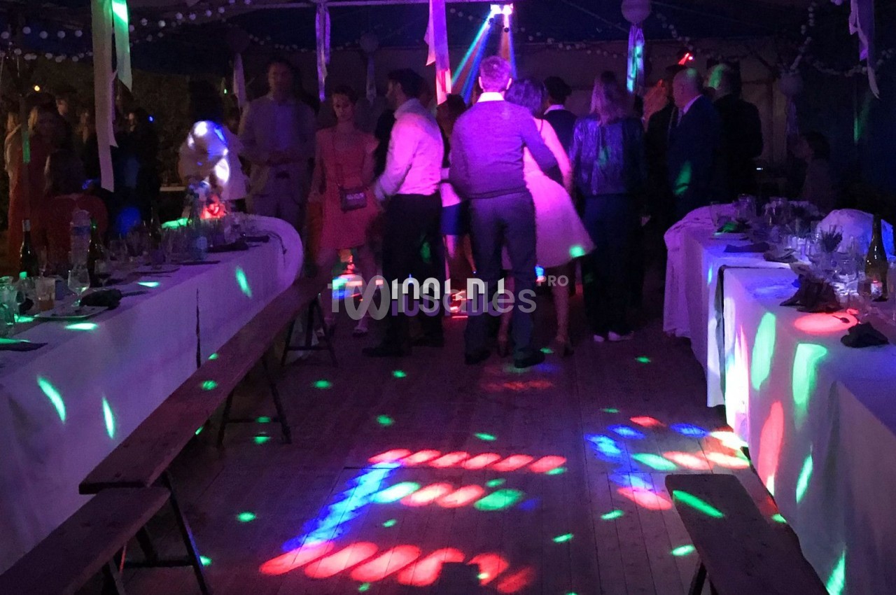 Personnes dansant sous un chapiteau éclairé par des lumières colorées, entourées de tables dressées.