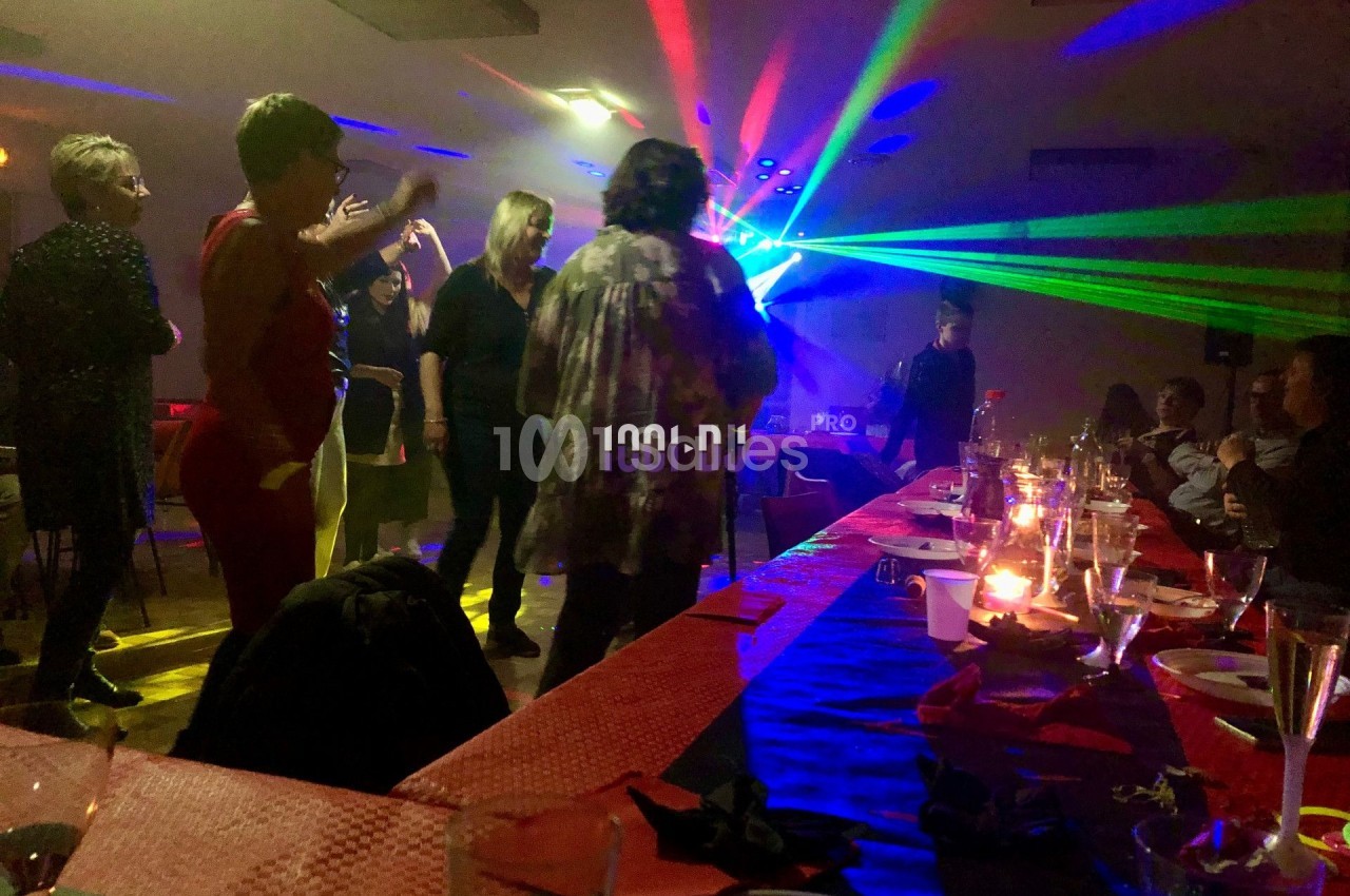 Des personnes dansent sous des lumières colorées dans une salle décorée avec des tables dressées.