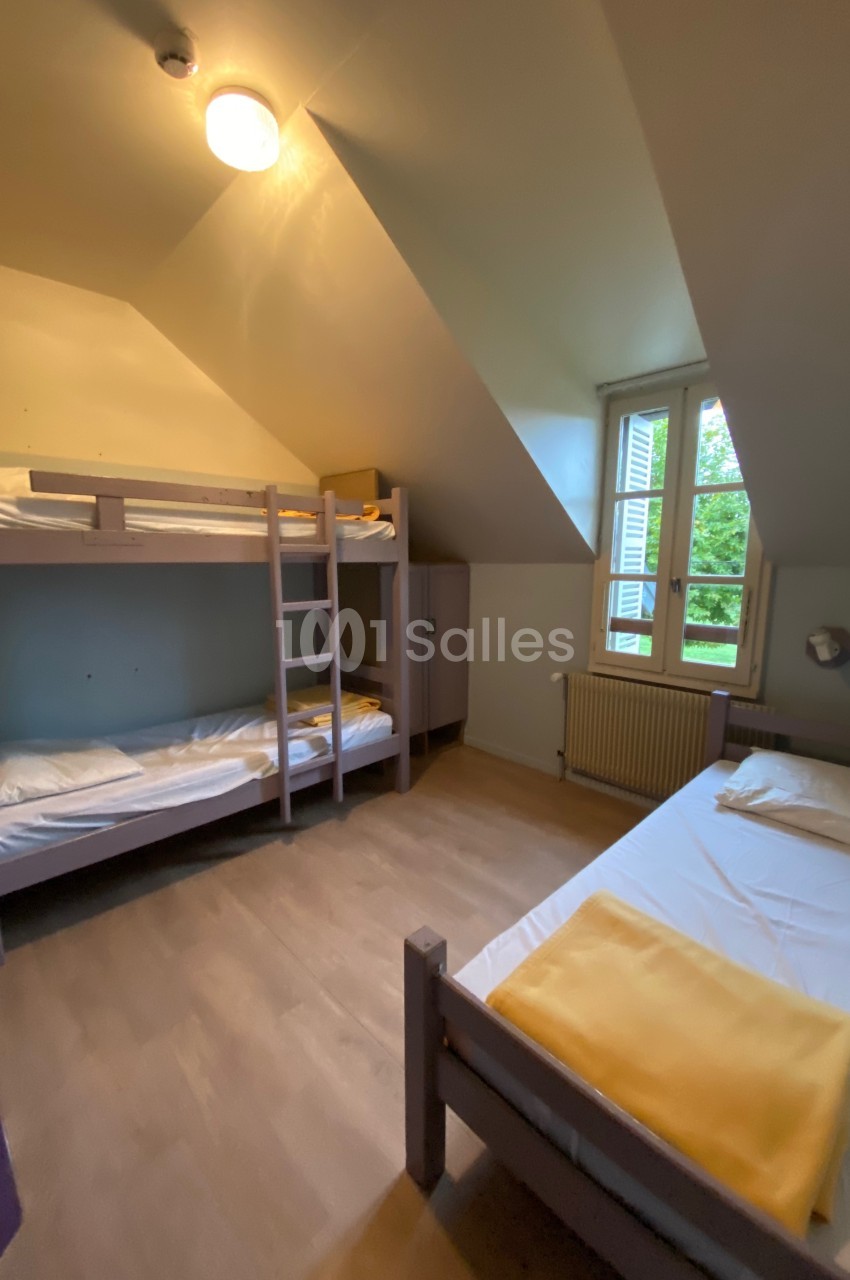 Chambre simple avec lits superposés, lit simple, fenêtre donnant sur un jardin, éclairage au plafond.