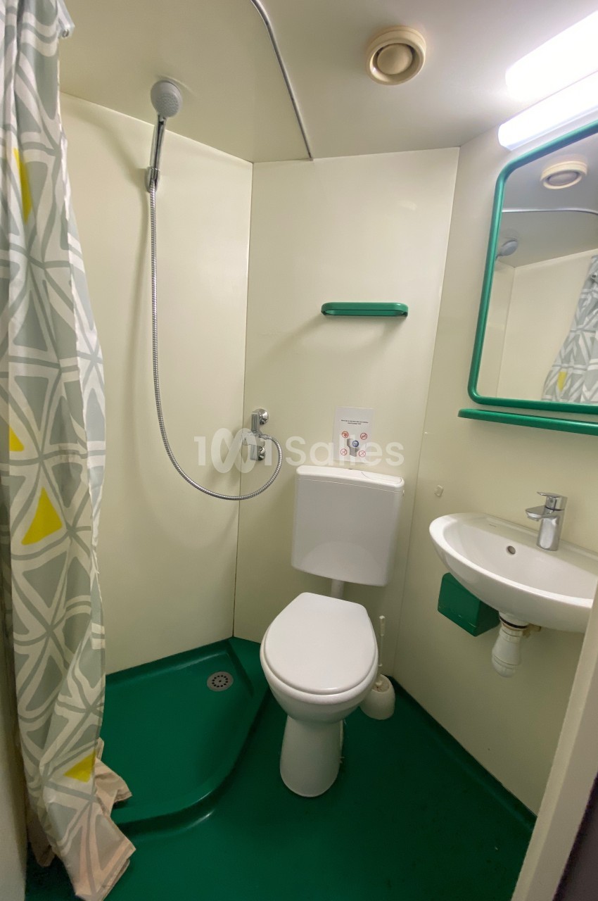 Salle de bain compacte avec douche, toilettes, lavabo, miroir et rideau de douche à motifs géométriques.