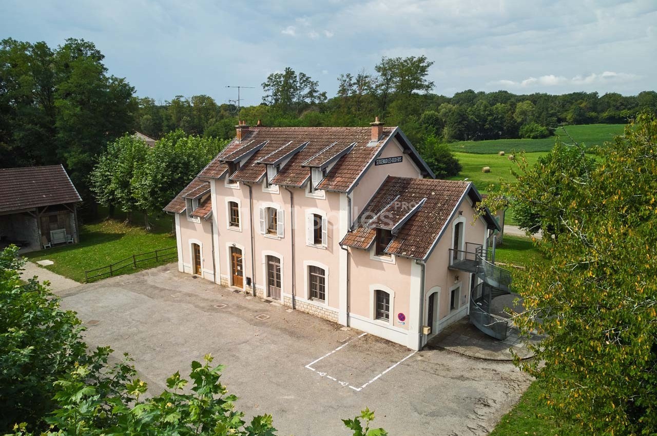 Bâtiment à deux étages avec façade rose, toit en tuiles et environnement rural verdoyant.