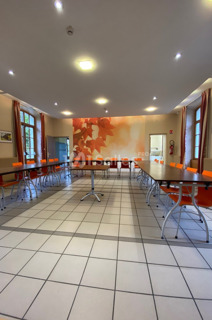 Salle de réunion lumineuse avec tables disposées en U, chaises orange et mur décoré de motifs de feuilles d'automne.