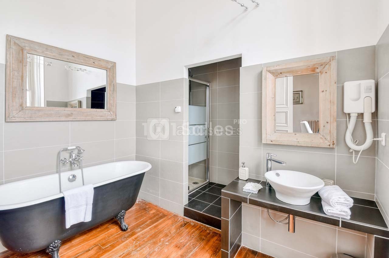 Salle de bain lumineuse avec baignoire sur pieds, douche à l'italienne, lavabo moderne et miroirs encadrés en bois.