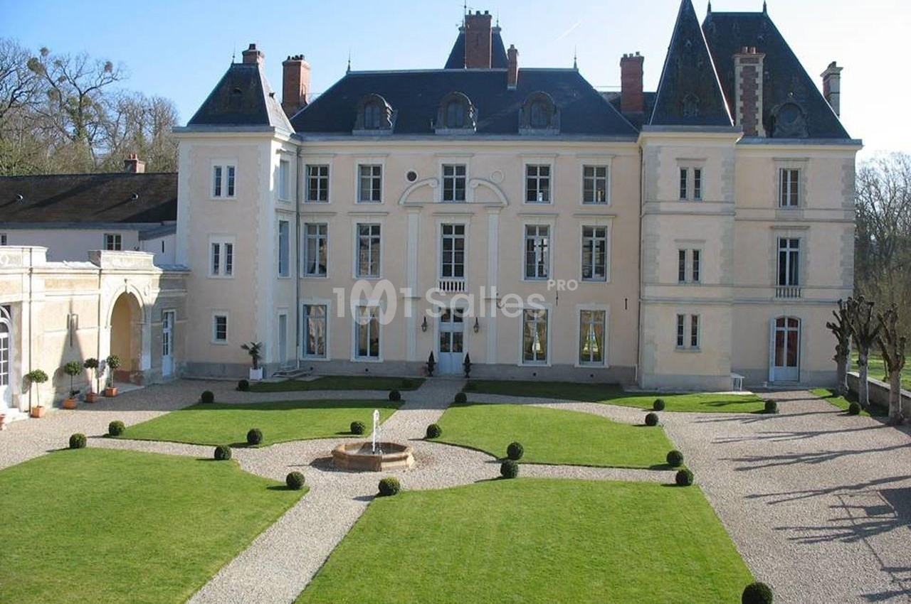 Façade d'un château avec toit en ardoise, entouré de jardins symétriques et allées gravillonnées.