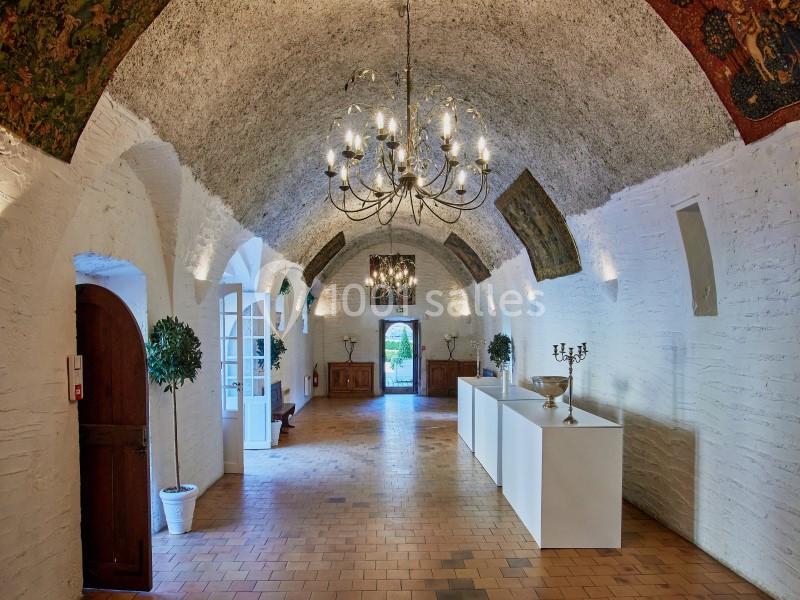 Salle voûtée avec murs blancs, lustres suspendus, sols en carreaux et décorations murales anciennes.