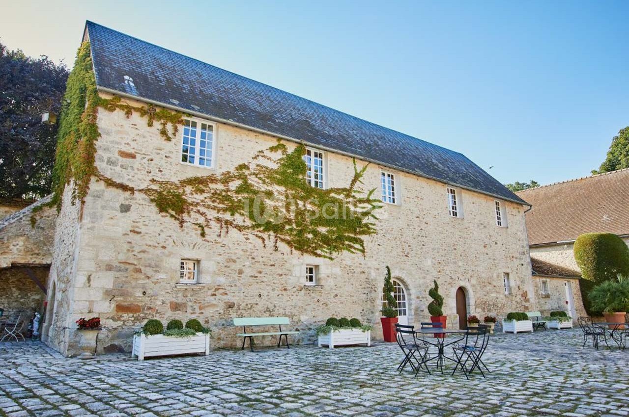 Bâtisse en pierre avec lierre grimpant, entourée d'une cour pavée et de mobilier de jardin.
