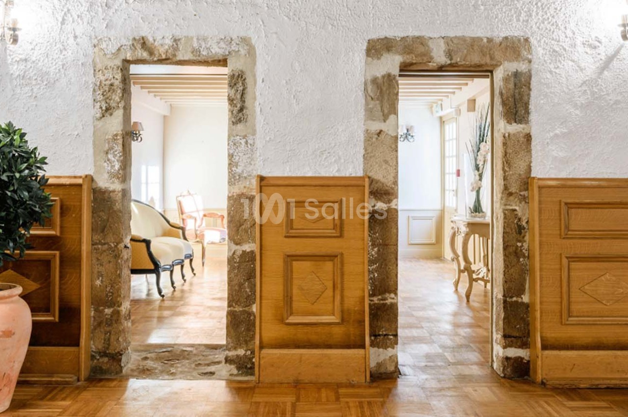 Deux portes en pierre et bois s'ouvrent sur des pièces lumineuses avec mobilier classique et parquet.