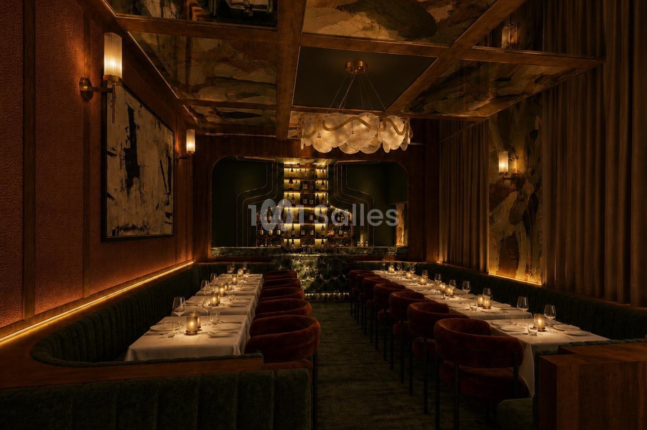Salle de restaurant élégante avec longues tables dressées, éclairage tamisé et bar illuminé en arrière-plan.