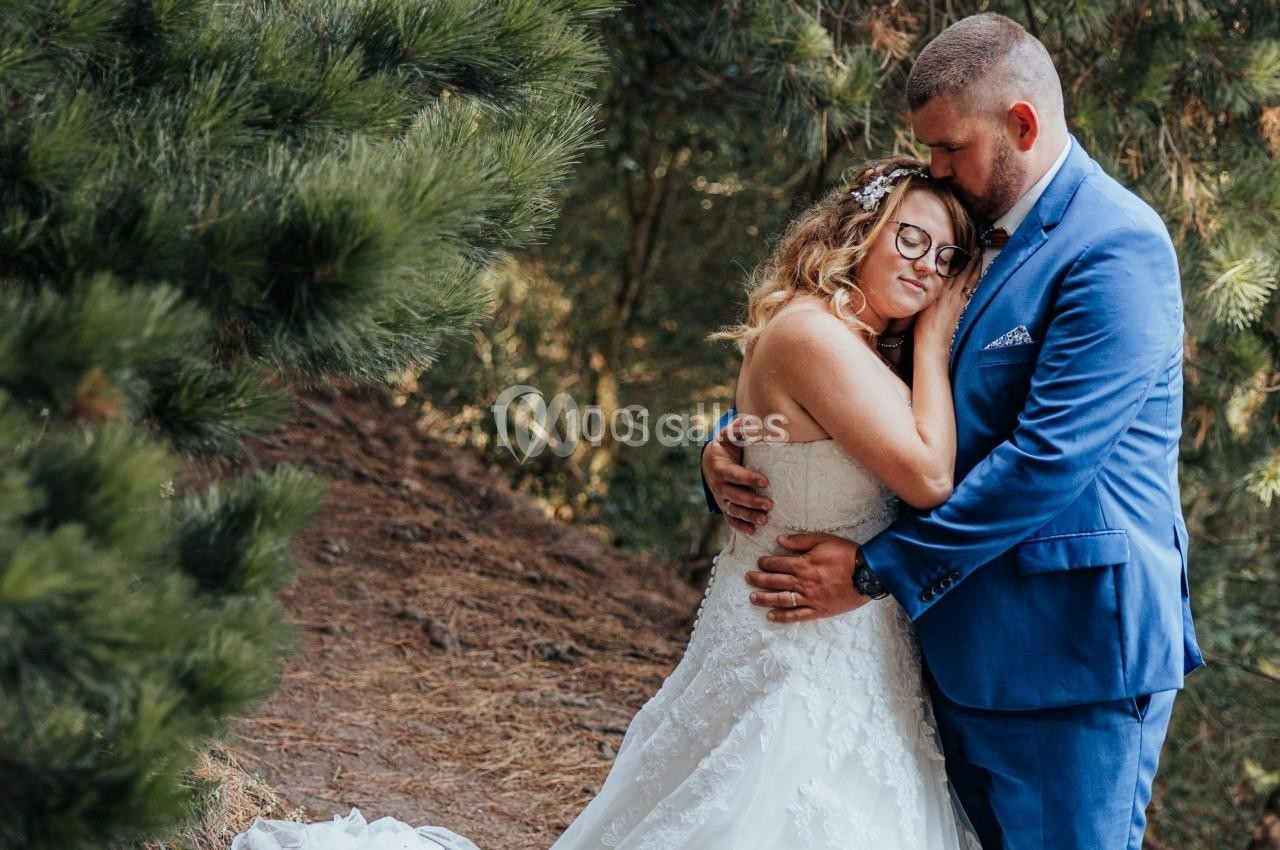 Un couple en tenue de mariage s'enlace tendrement dans une forêt, entouré de pins.