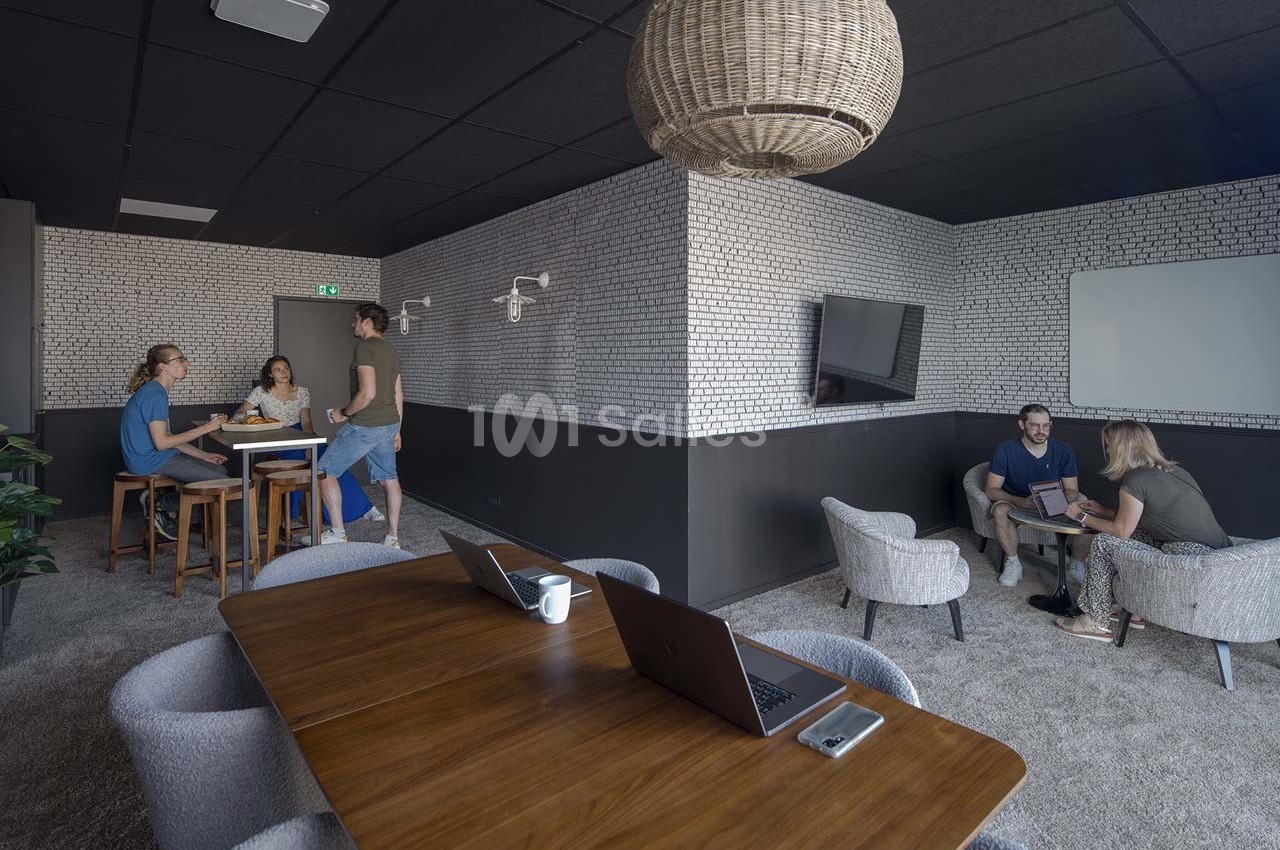 Espace de travail partagé avec tables, chaises, ordinateurs et personnes discutant dans une ambiance moderne et lumineuse.