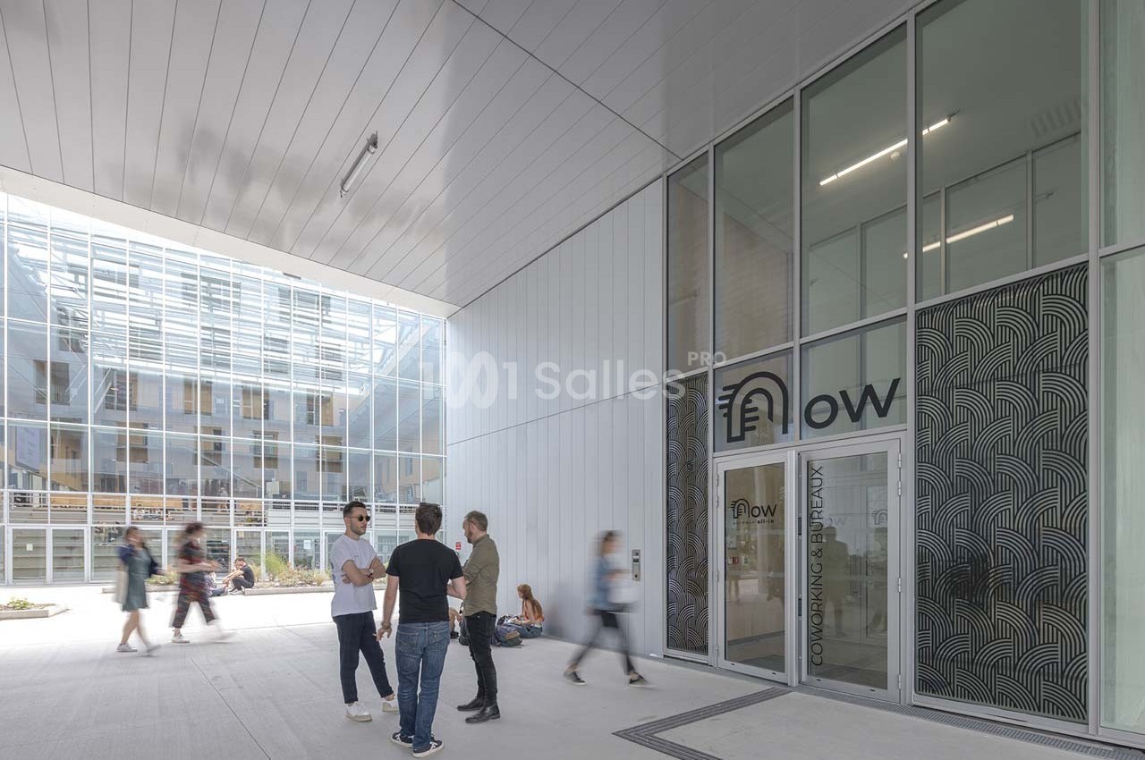 Entrée d'un espace de coworking moderne avec des personnes discutant dans une cour lumineuse.