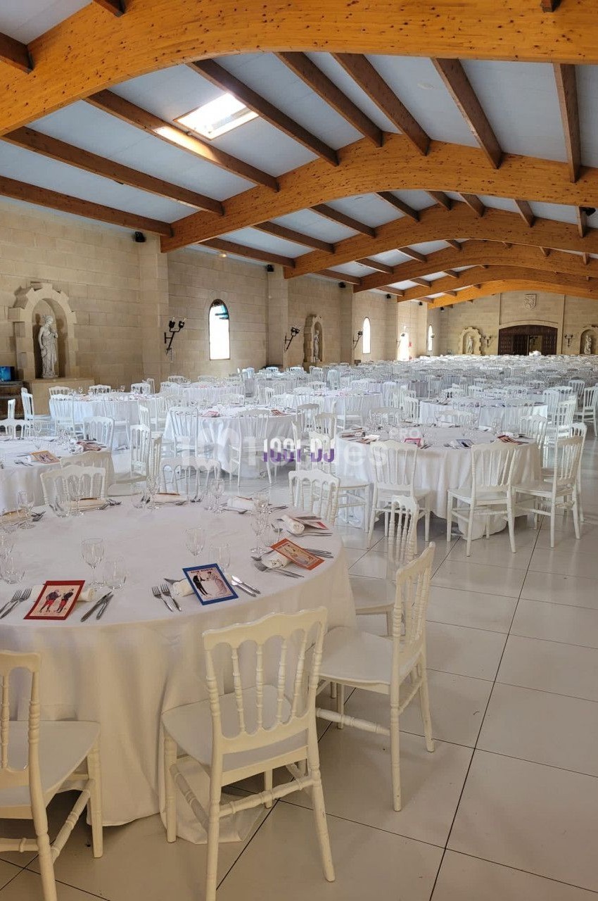 Salle de réception lumineuse avec tables rondes dressées, nappes blanches et chaises en bois clair.