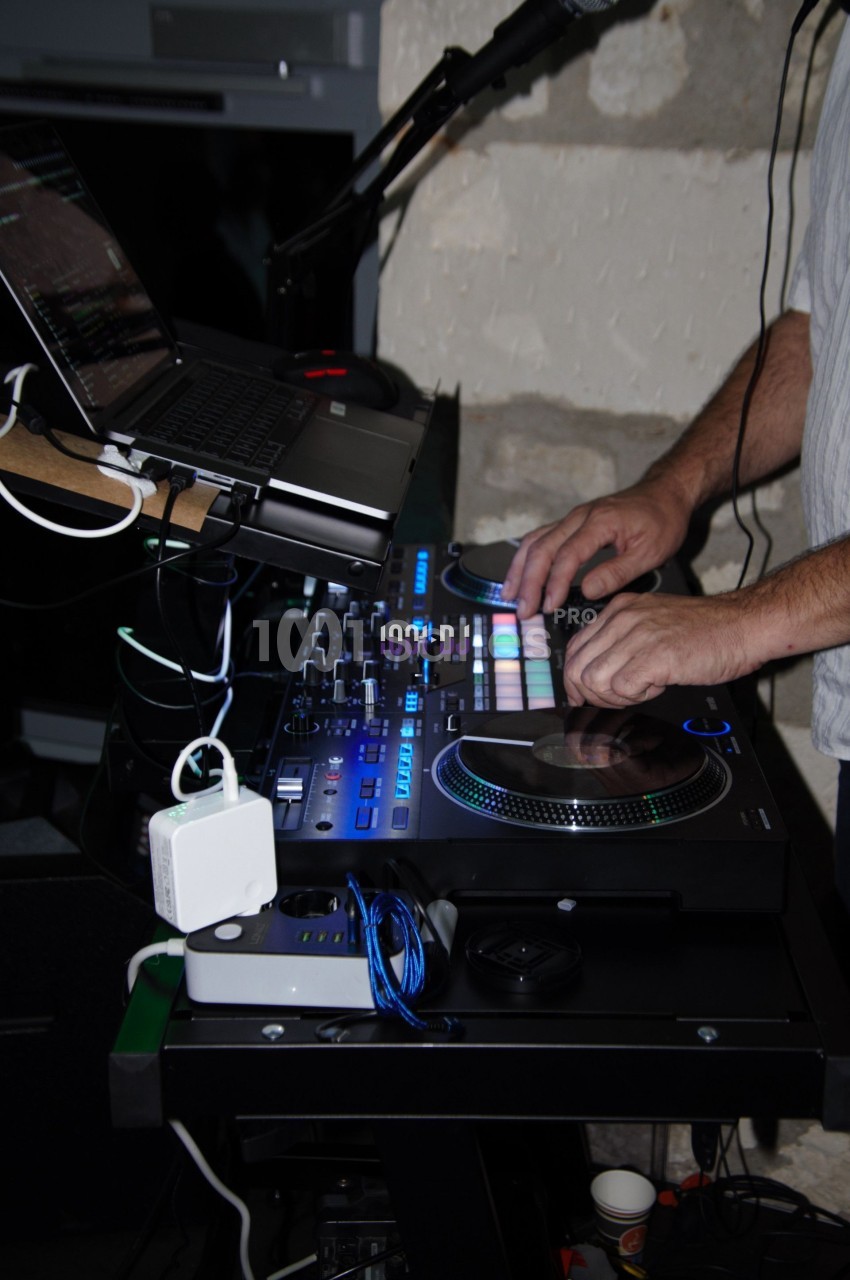 Un DJ manipule une table de mixage équipée de lumières colorées, avec un ordinateur portable posé dessus.