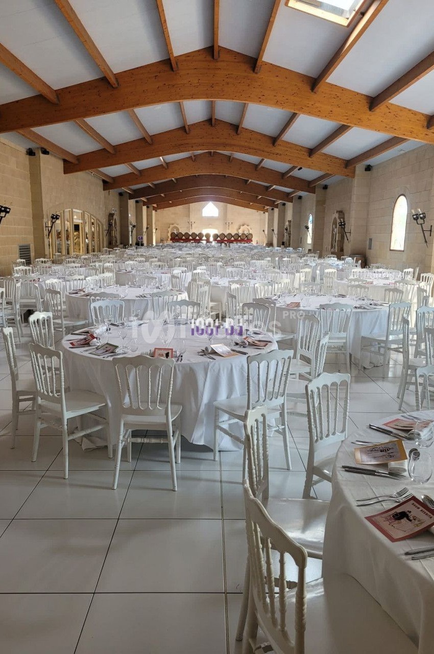 Salle de réception spacieuse avec des tables rondes dressées, nappes blanches et chaises alignées.
