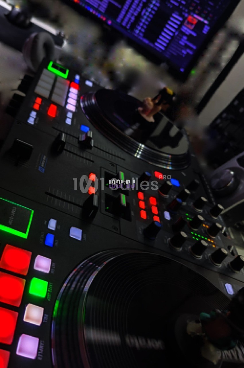 Table de mixage avec platines et boutons lumineux, accompagnée d'écrans affichant des interfaces de mixage audio.