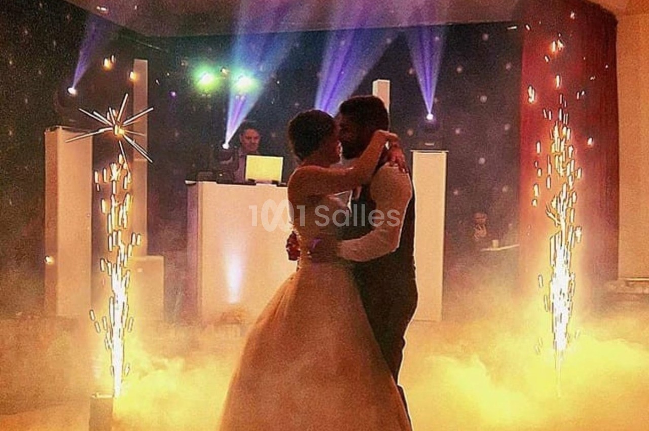 Un couple danse dans une ambiance festive avec éclairages colorés, fumée et étincelles décoratives.