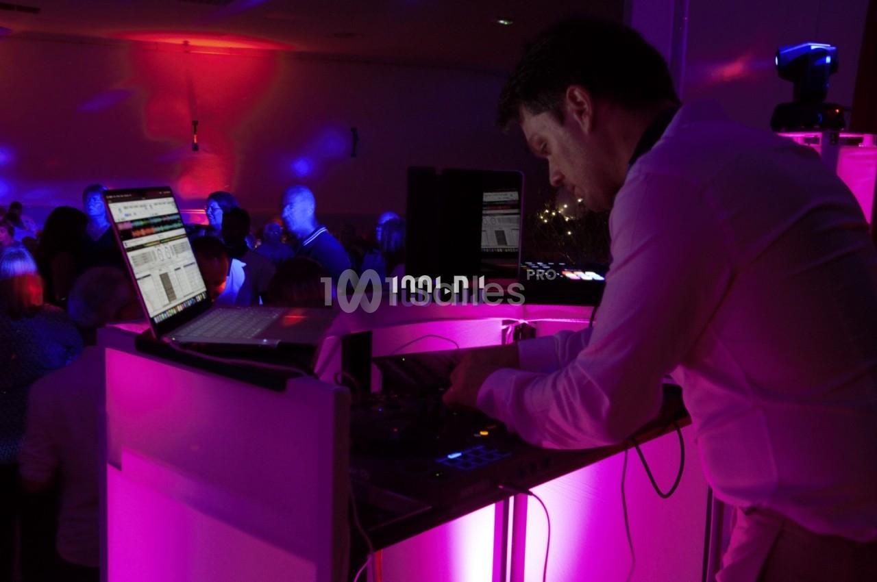 Un DJ mixe de la musique sur une console éclairée par des lumières colorées dans une salle sombre.