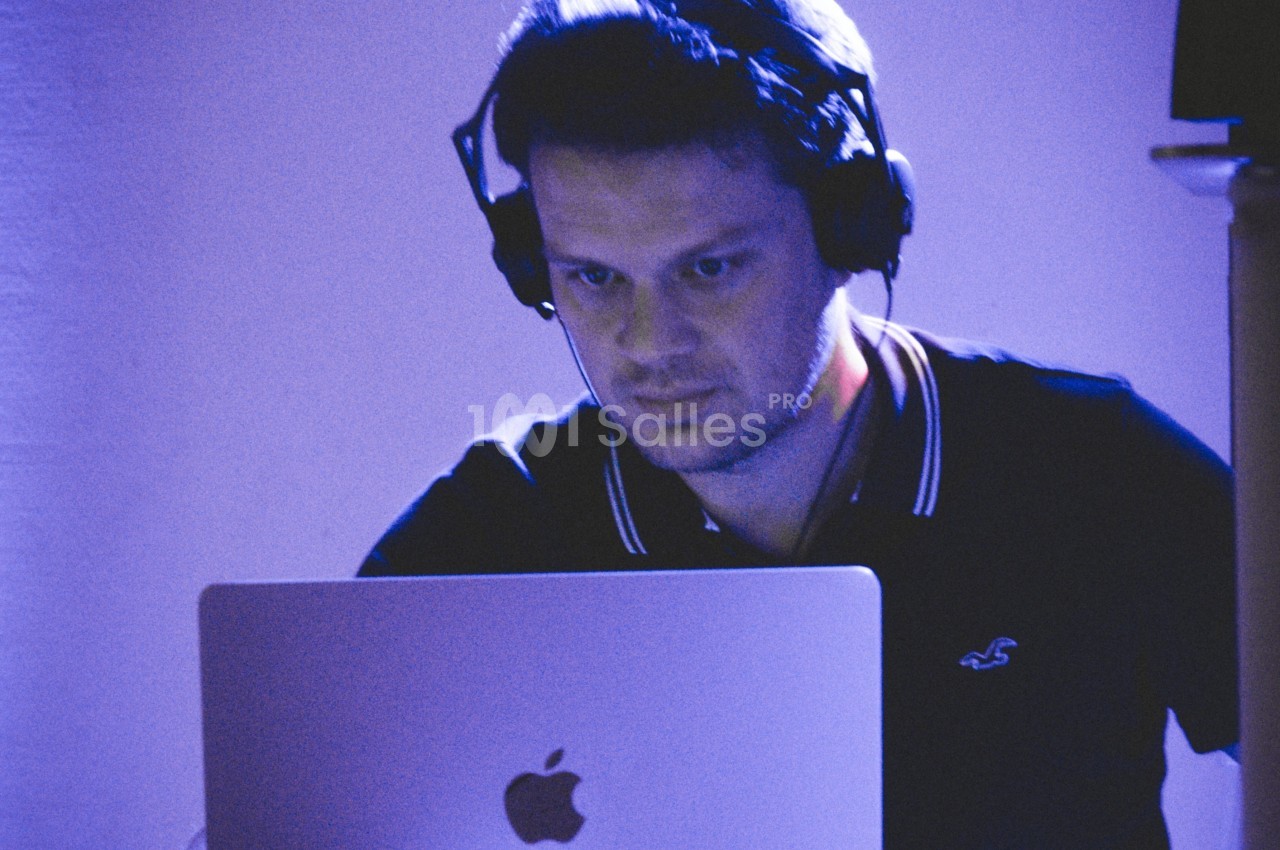 Homme portant un casque audio, concentré sur un ordinateur portable dans une ambiance lumineuse bleutée.