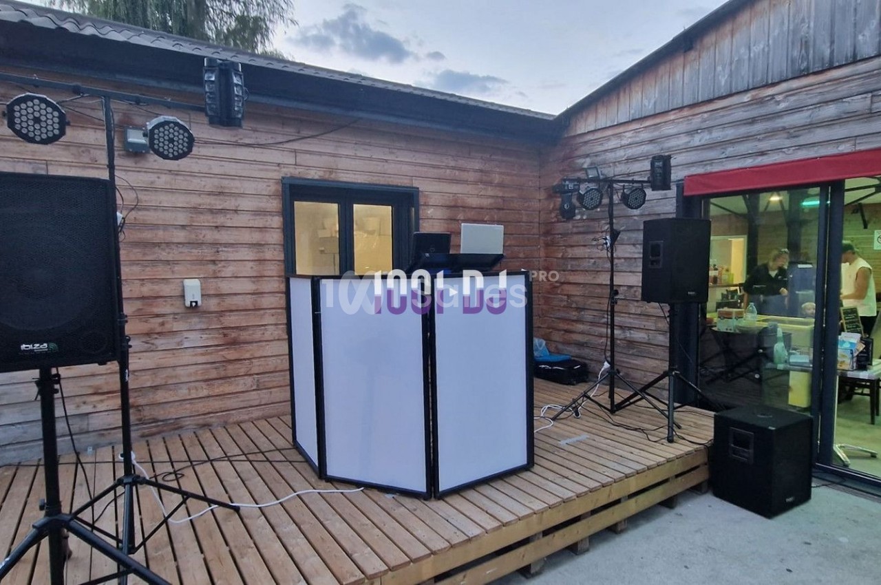 Installation de matériel DJ avec enceintes et éclairages sur une terrasse en bois devant un bâtiment.