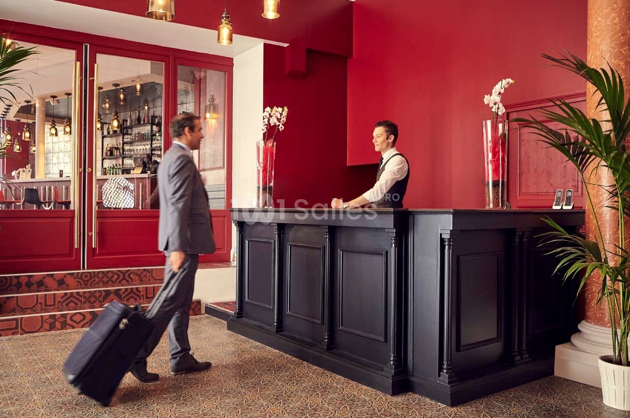 Un homme en costume avec une valise s'approche du comptoir de réception d'un hôtel au décor élégant et chaleureux.