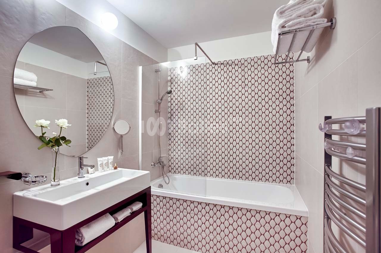 Salle de bain avec baignoire, carrelage à motifs, lavabo avec miroir ovale, et porte-serviettes mural.