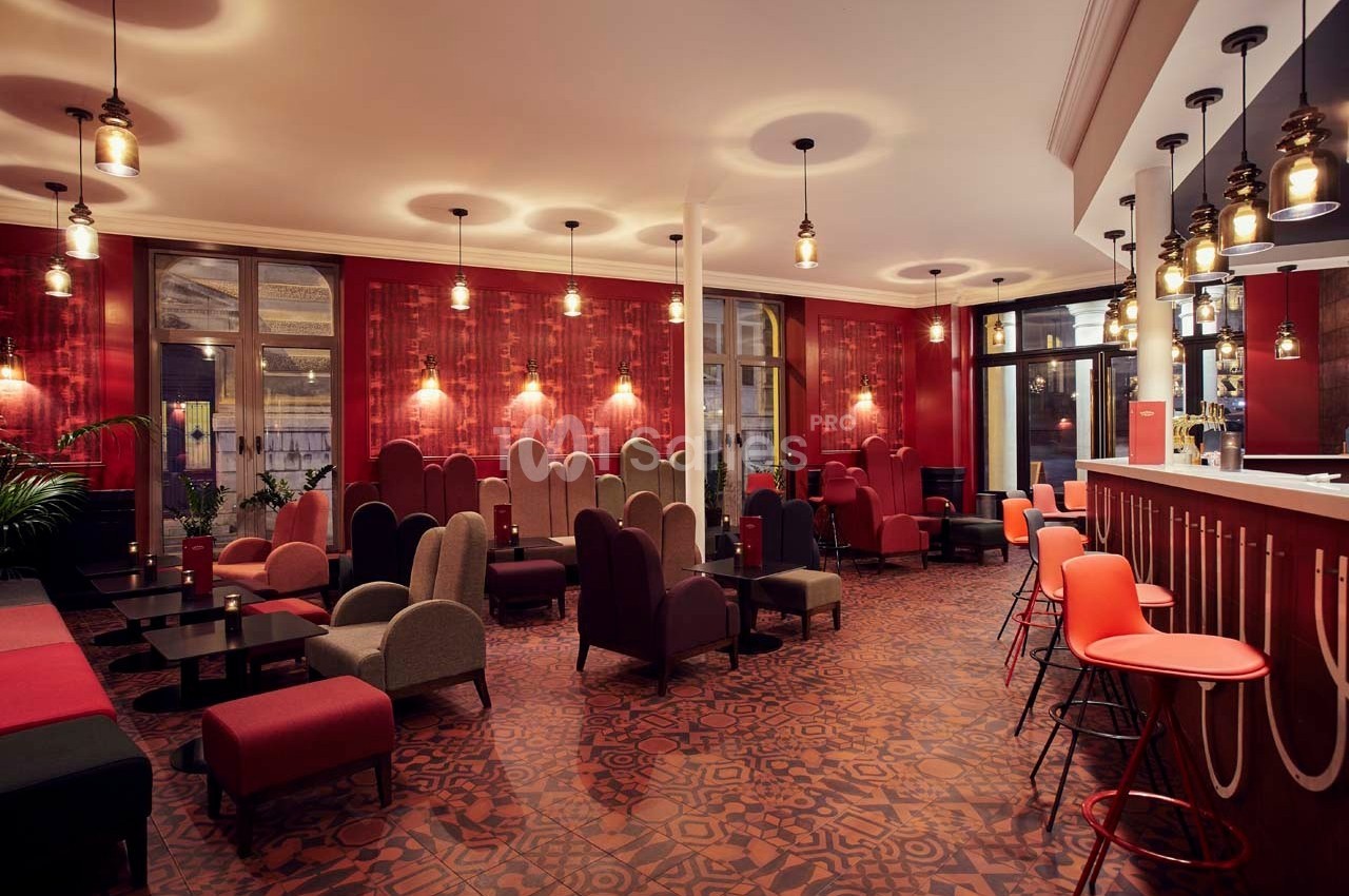 Salle lumineuse avec fauteuils colorés, tables basses, bar moderne et décor rouge chaleureux.